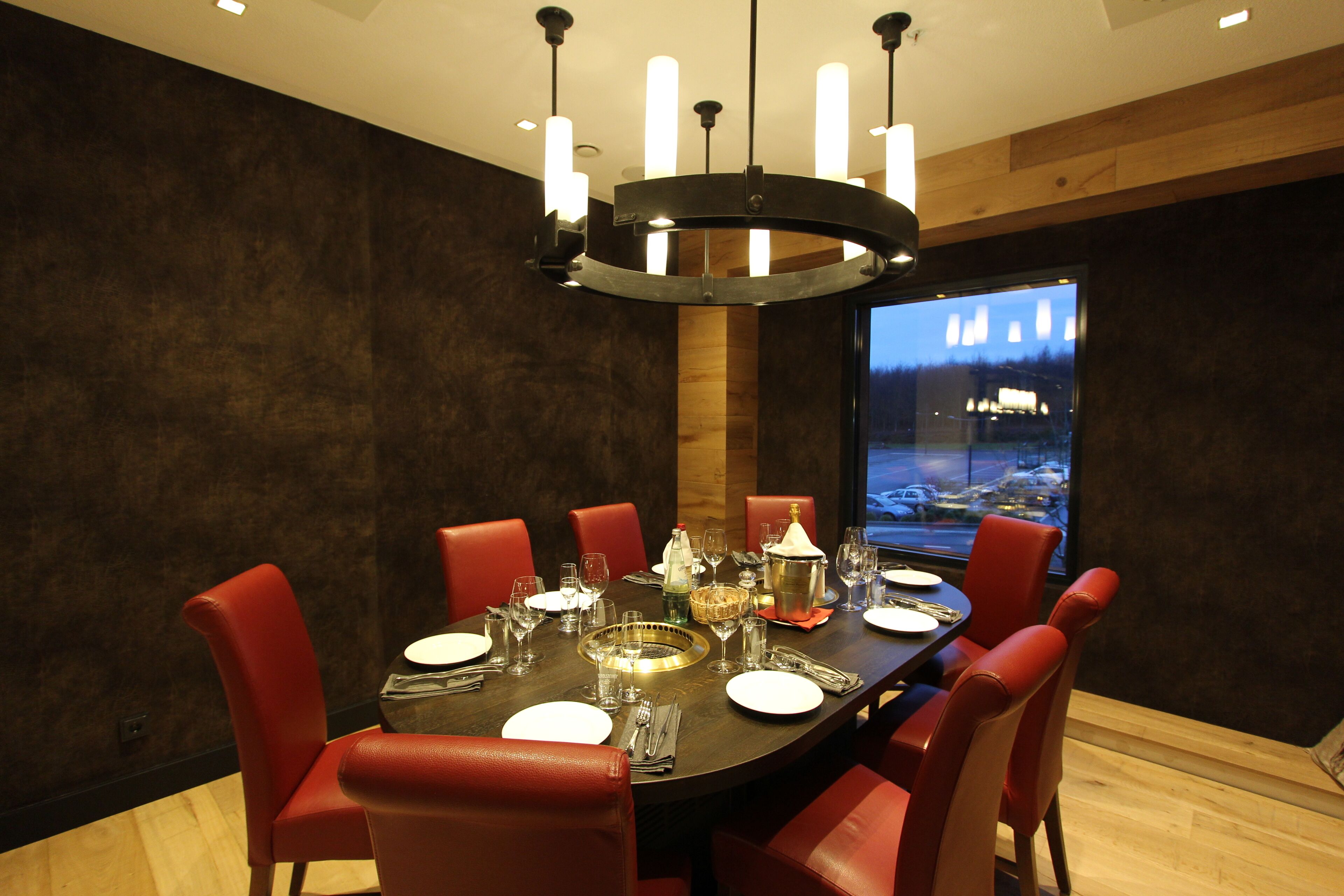 A dining area with a round table set for six, red chairs, a chandelier, and a view of a snowy landscape through a large window.