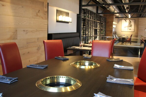 A restaurant with a wooden wall, red chairs, a black table, and a wine rack in the background.