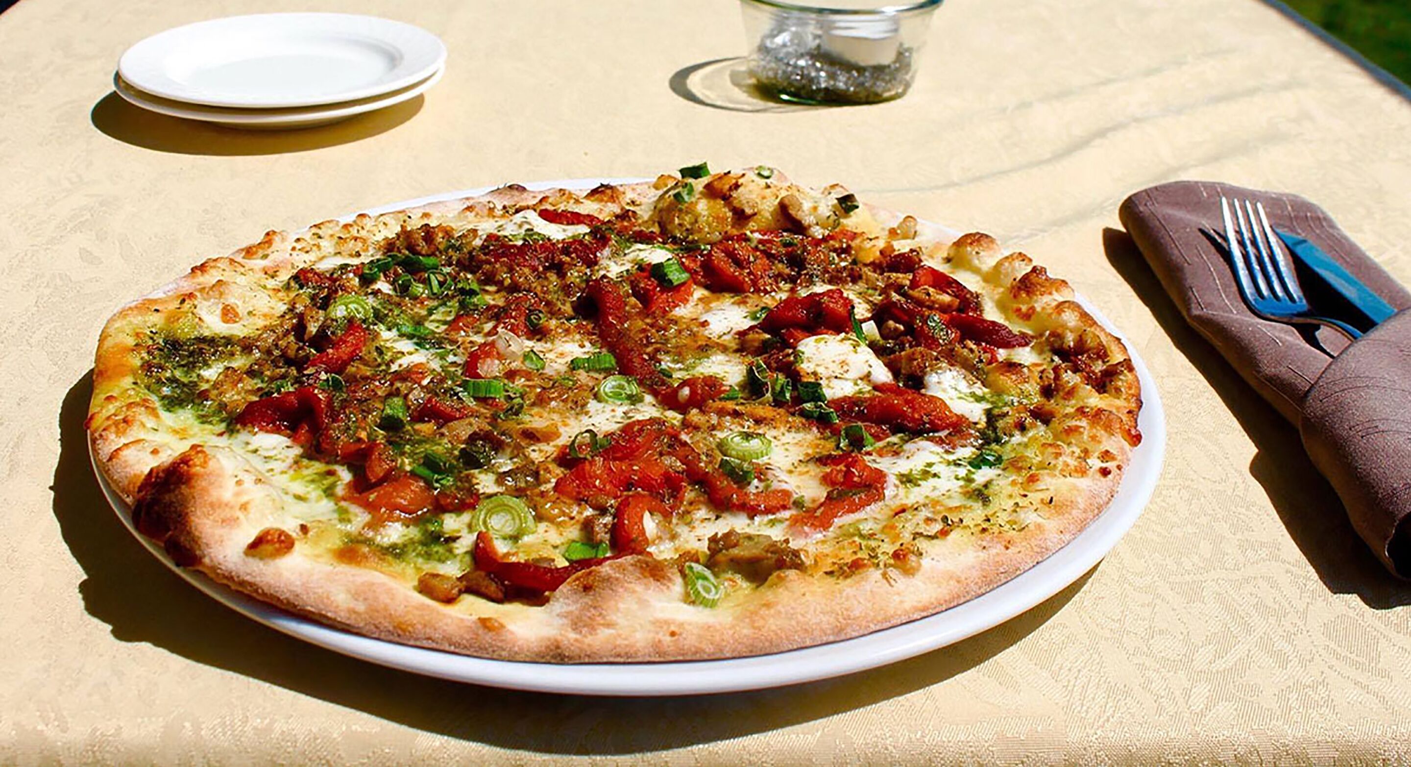 A pizza on a white plate with a napkin and fork on the right.