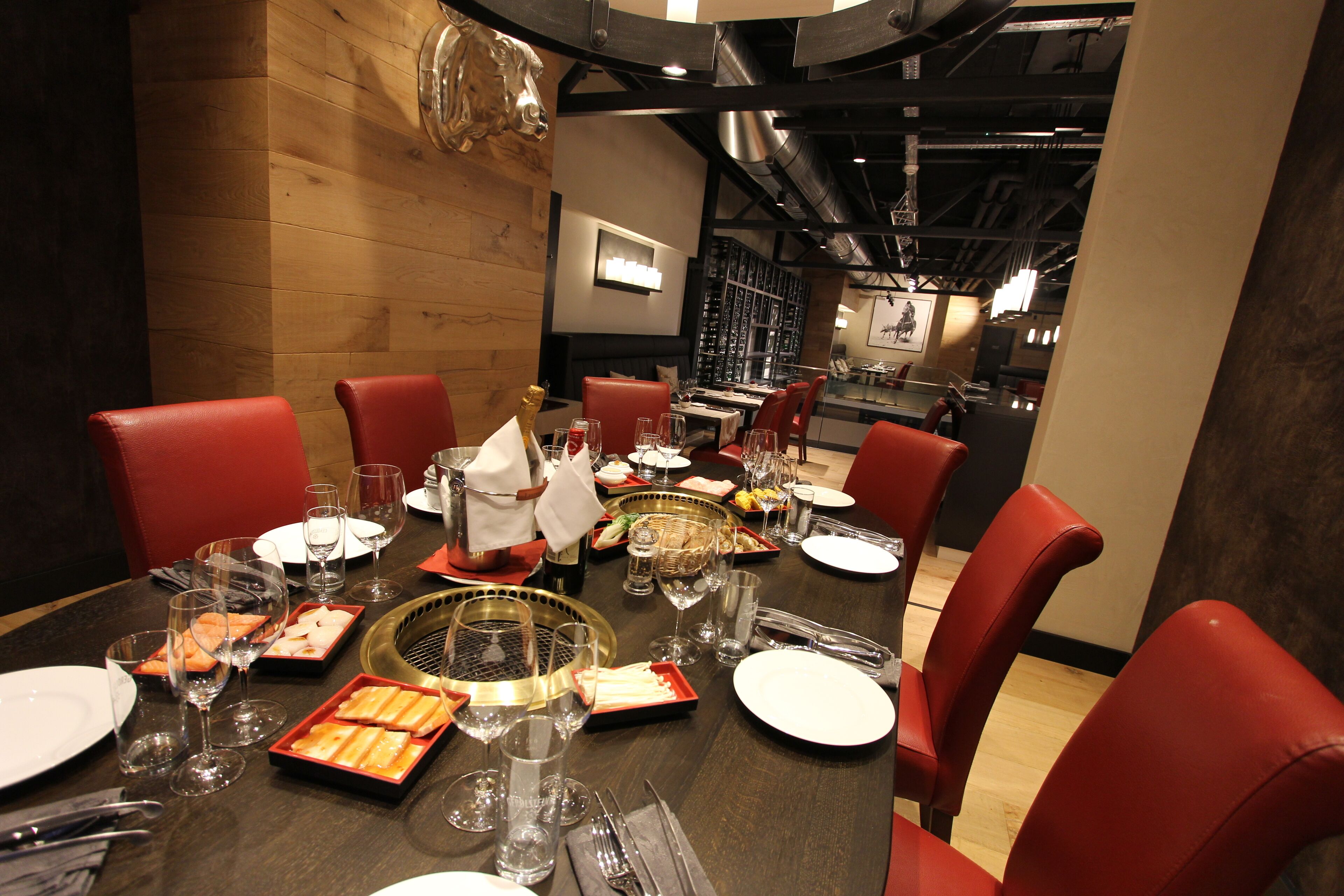 Un espace repas avec un mur en bois, des chaises rouges, une table ronde dressée avec des assiettes, des verres et un grill chaud.