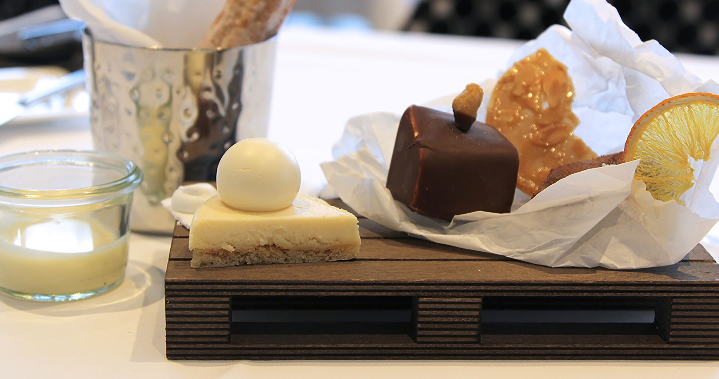 A dessert tray with various sweets and a glass of cream.