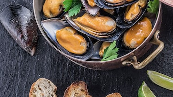 A pot of mussels with bread and lime wedges on a dark surface.