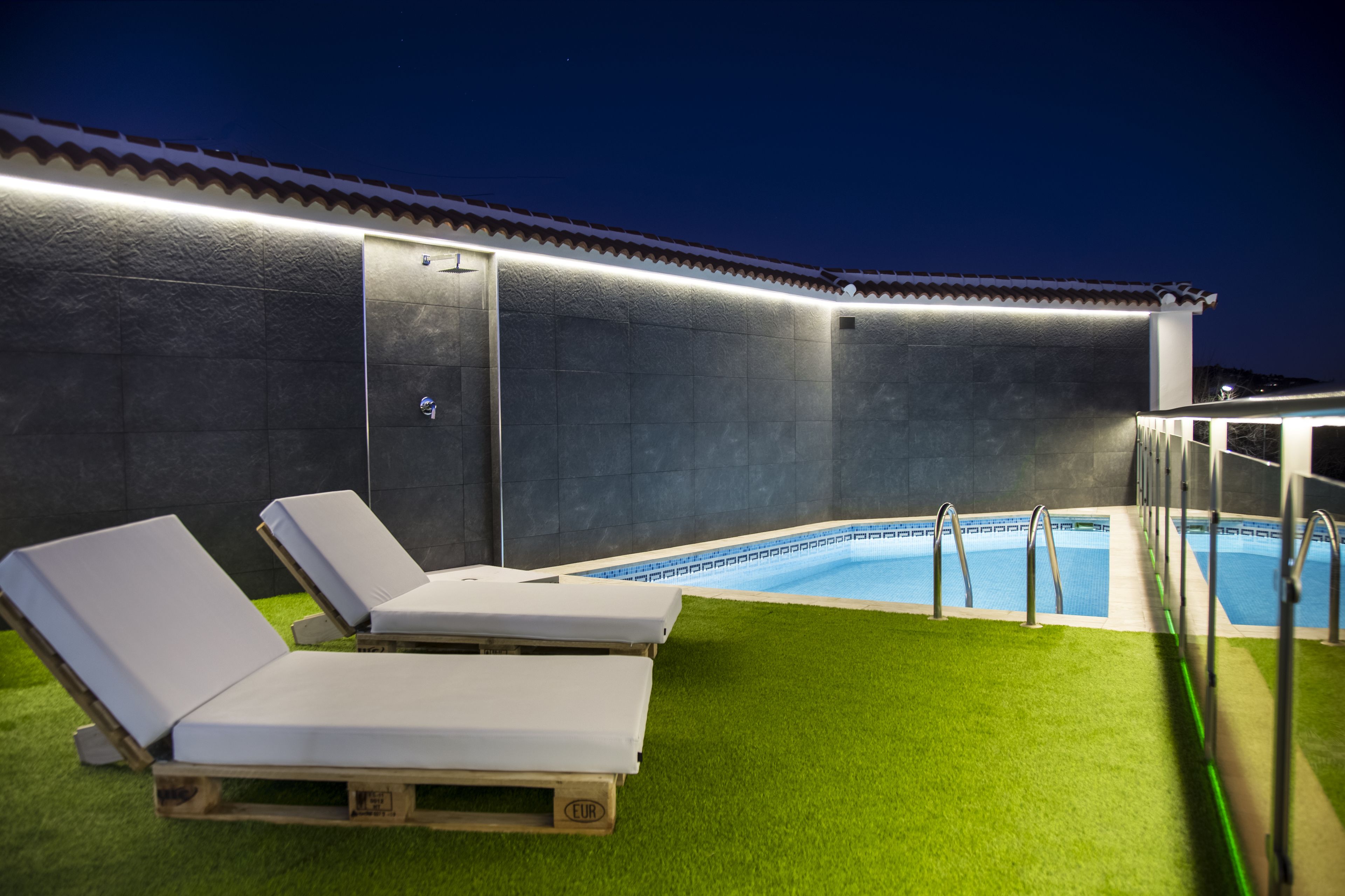 Zona de piscina exterior amb dues cadira relaxants i una zona de seients coberta.