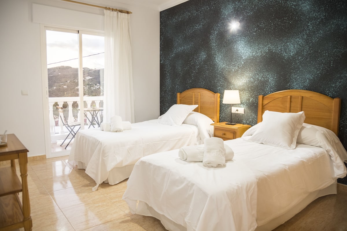 A hotel room with two beds, a balcony with a view, and a starry night wall.