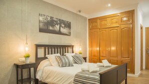 A neatly made bed with a striped bedspread, a bedside table with a plant, and a wall-mounted painting. - HR Mirador (Canillas de Albaida)