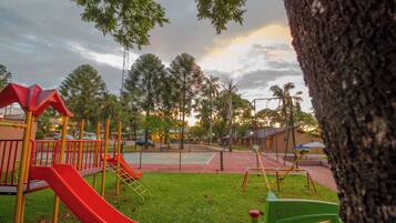 Children can play on the playground's slide and climbing structures amidst a lush lawn and trees.