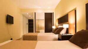 Habitación de hotel con dos camas, televisor montado en la pared y una mesita de noche con lámpara.