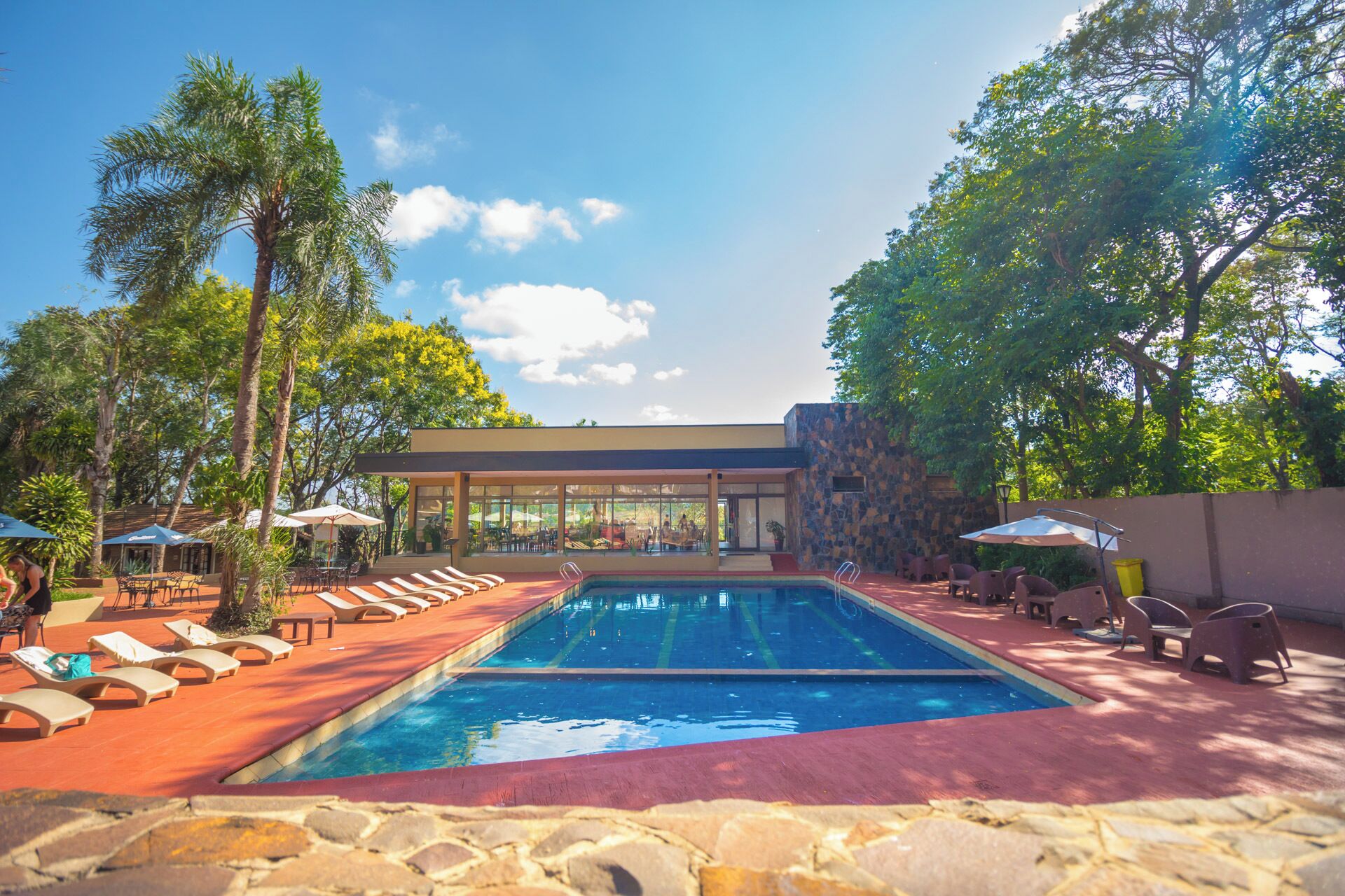 Un área de piscina con sillones de descanso, una zona de estar cubierta y un muro de piedra.
