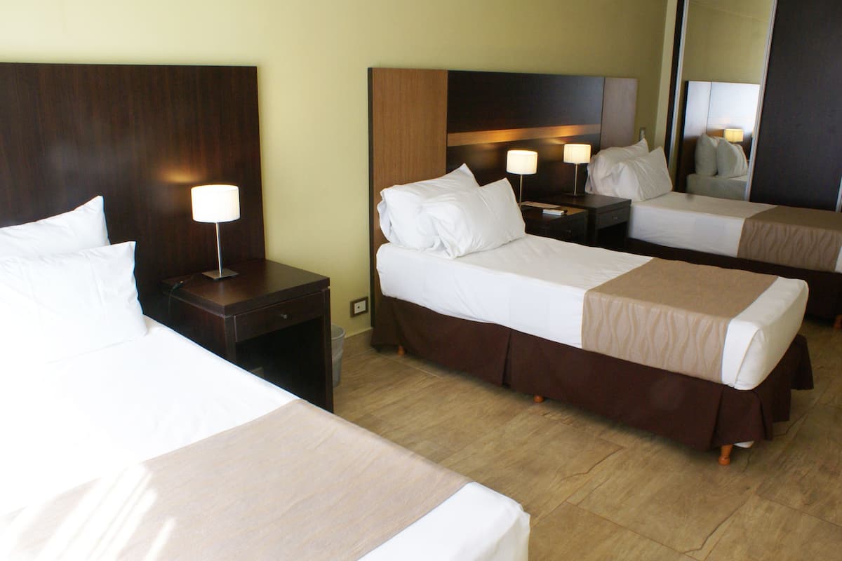 A hotel room with two beds, a wooden headboard, a nightstand with a lamp, and a mirror.