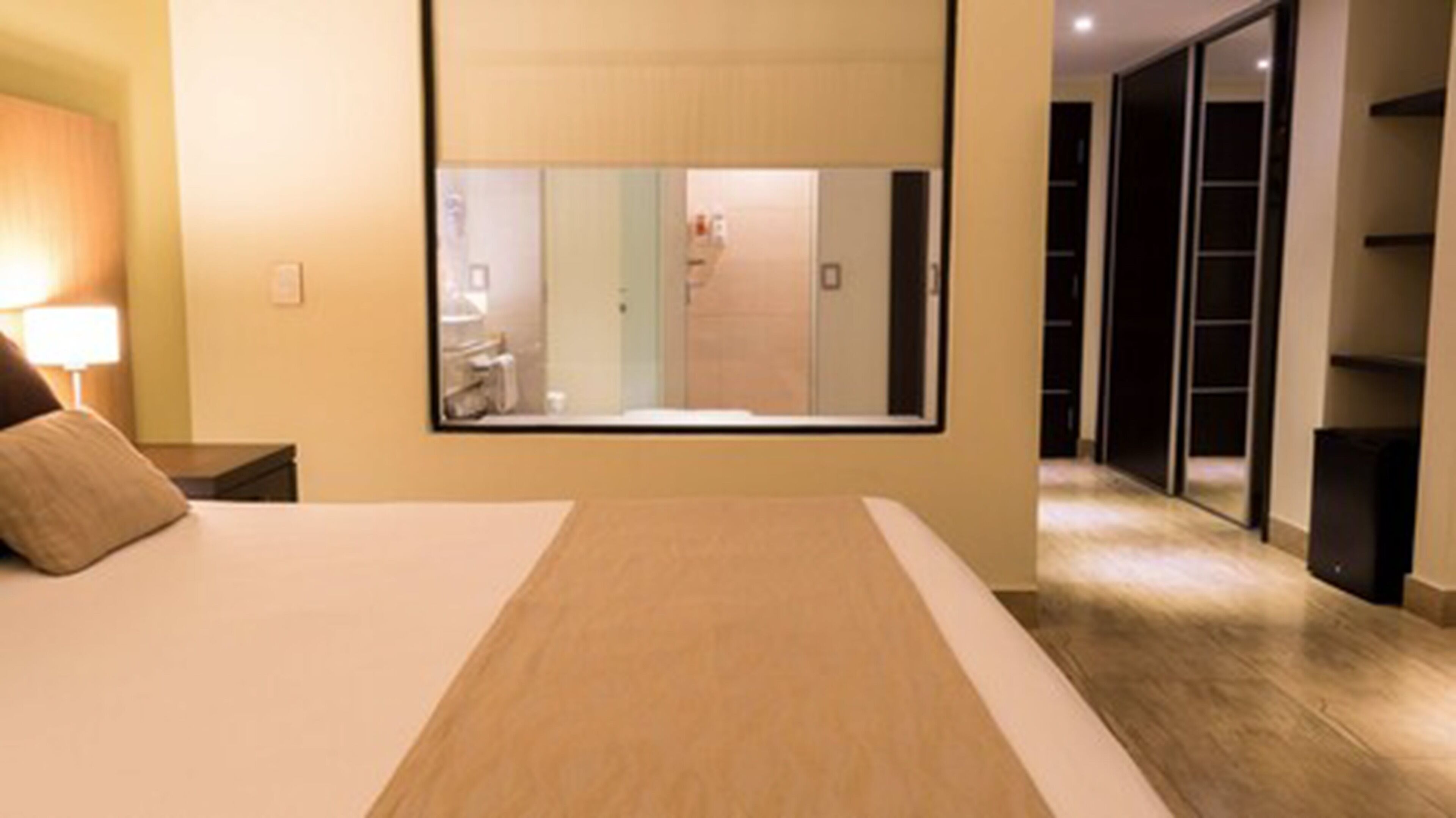 A hotel room with a large bed, a nightstand, a mirror, and a view of the bathroom and closet.