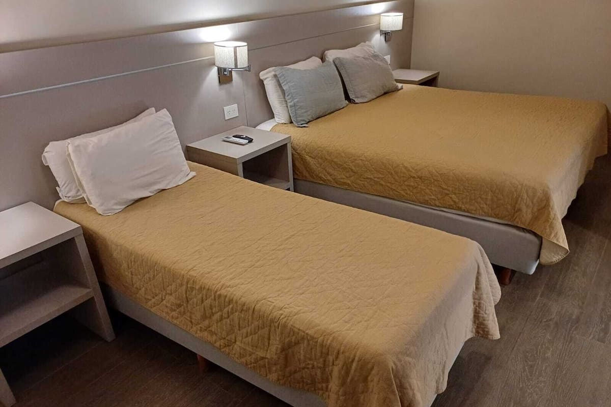 A hotel room with two single beds, each with a headboard, bedside tables, and lamps.