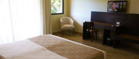 A hotel room with a bed, a desk, a chair, a television, and an air conditioning unit.