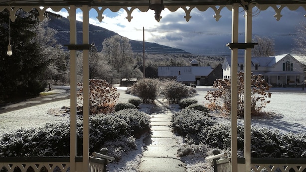 A covered porch with a view of a snow-covered landscape, including a pathway and buildings in the distance.
