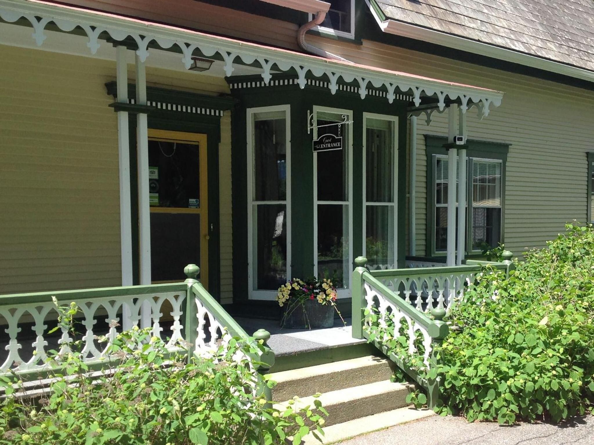 A green building with a porch, a sign reading "Entrance," and steps leading to the door.