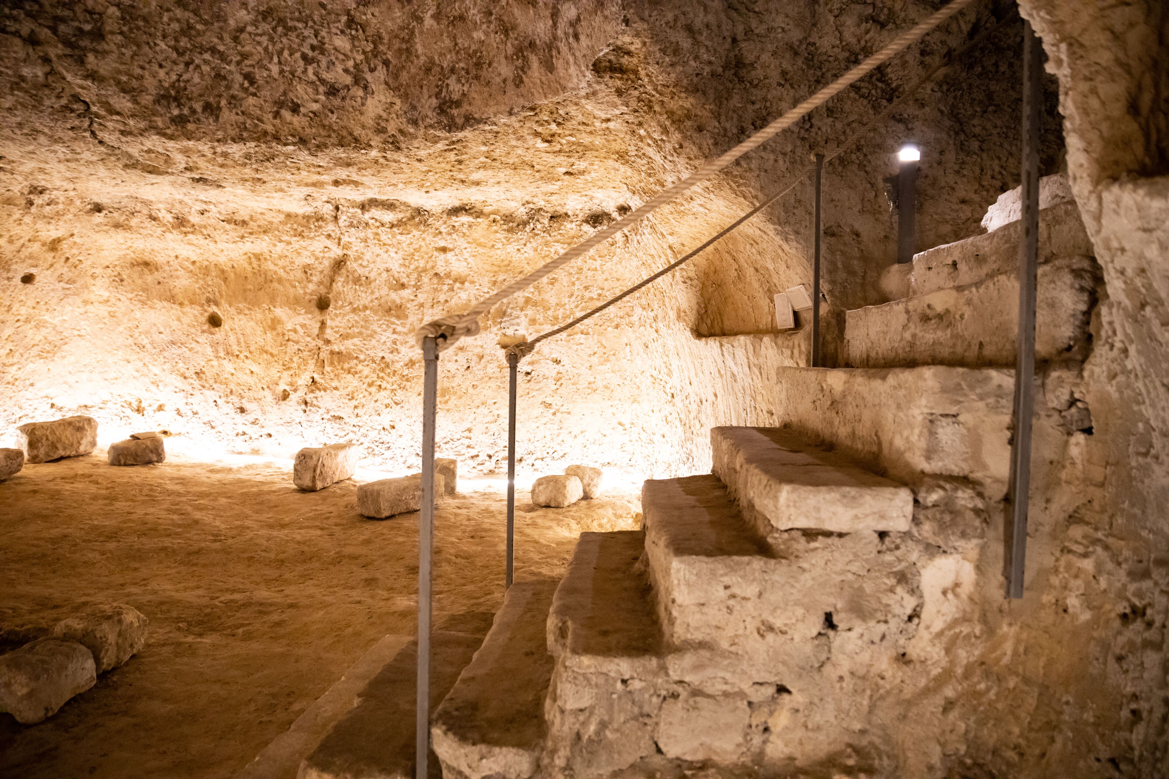 A stone staircase in a cave-like structure with metal railings and a light source at the top.