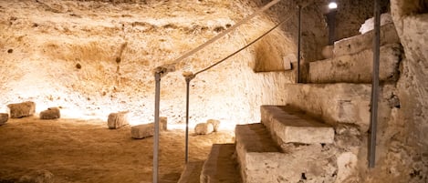 A stone staircase in a cave-like structure with metal railings and a light source at the top.