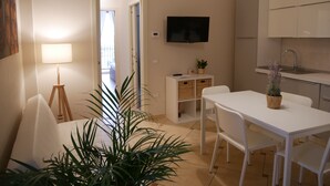 Una cocina moderna con armarios blancos, un televisor de pantalla plana, una mesa de comedor con sillas y una planta en maceta.