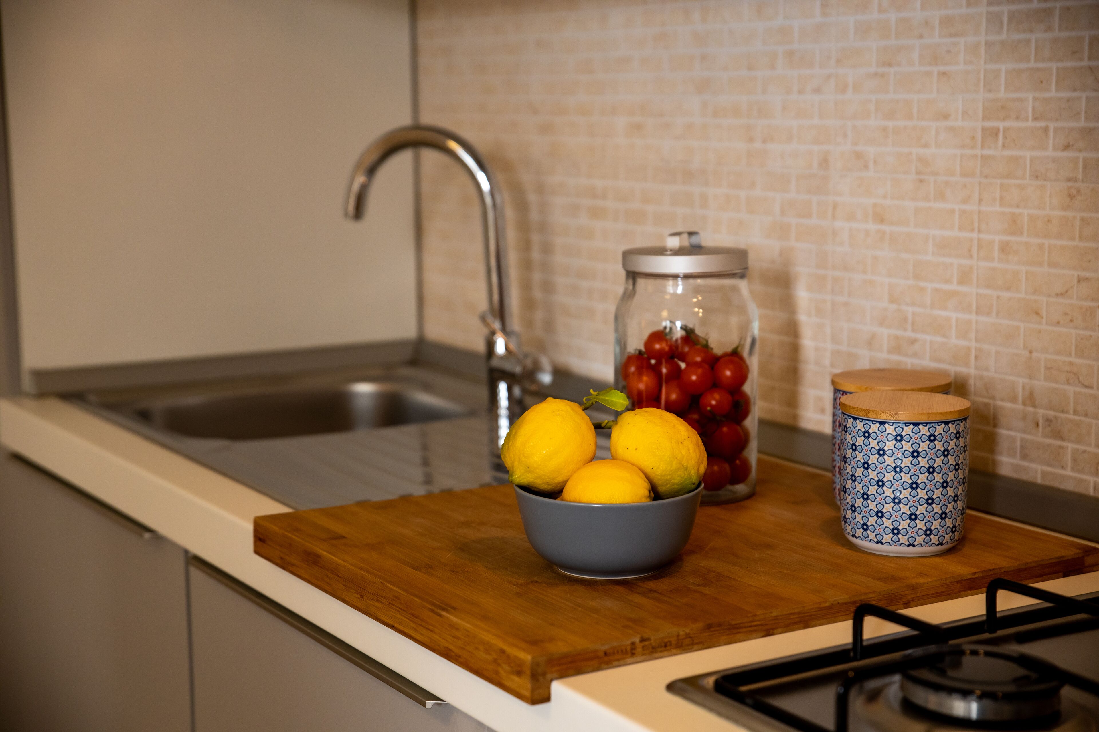 Una encimera de cocina con un bol de limones y tomates, un tarro de tomates, y un recipiente azul y blanco estampado.