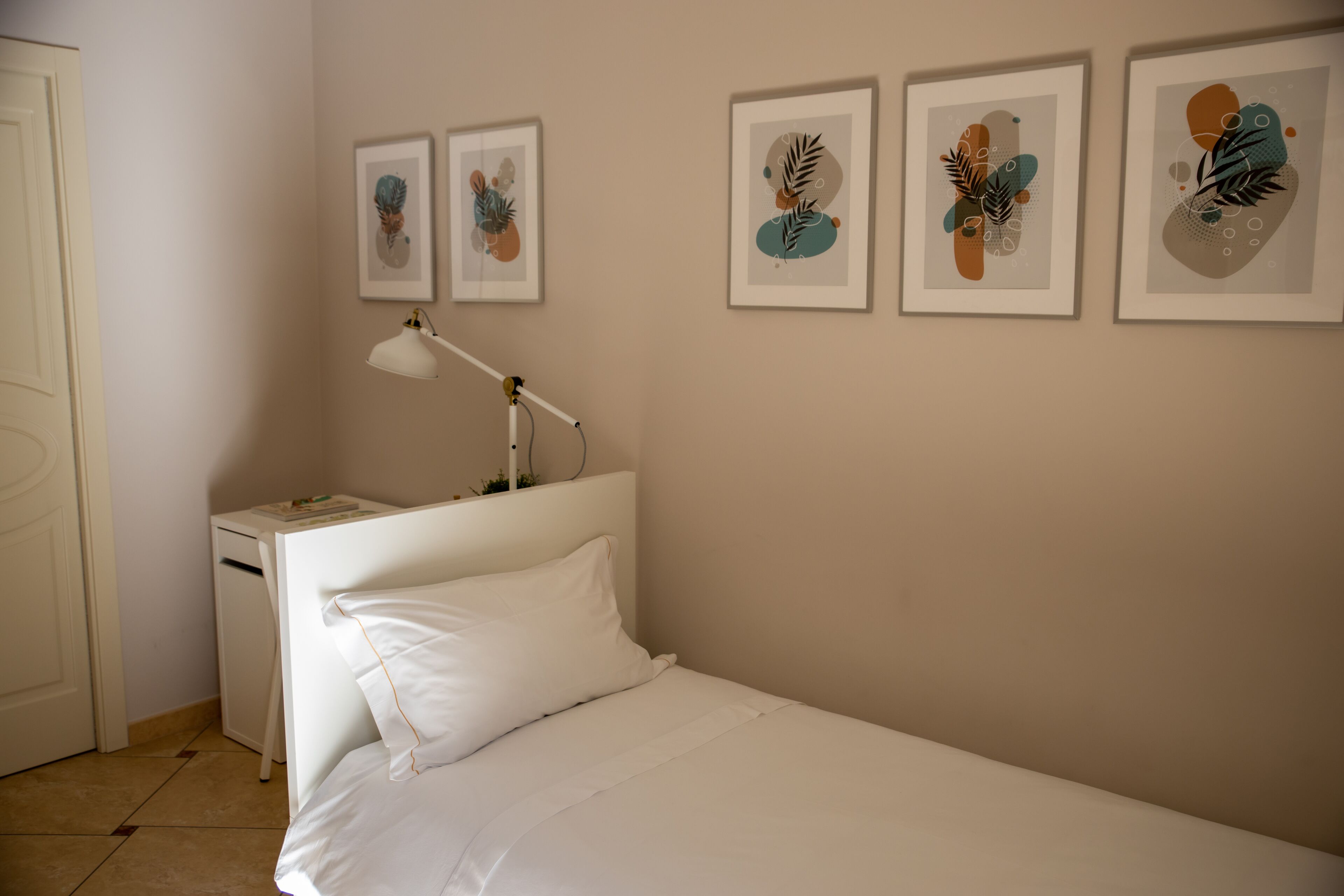 A bedroom with a bed, a bedside table with a lamp, and three framed artworks on the wall.