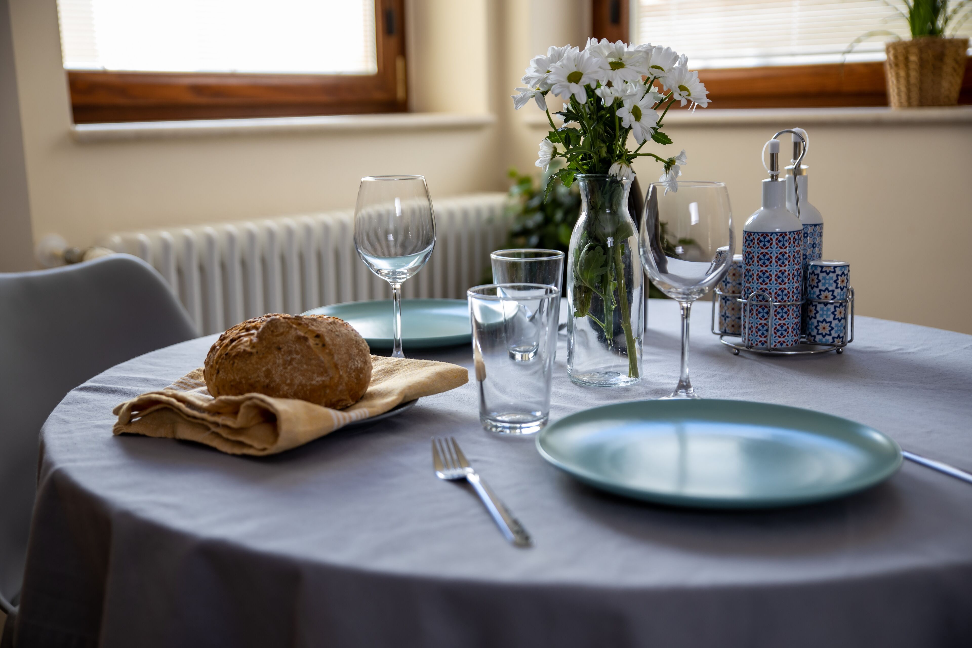 A dining table with a loaf of bread, a plate, a glass, a vase with flowers, and a salt and pepper set.