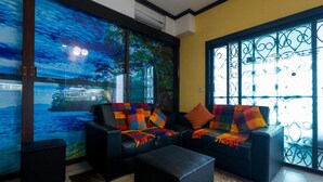 Una sala de estar con dos sofás negros, una manta colorida y un ventanal con vista al mar.