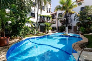 A swimming pool surrounded by lush greenery and a white building with balconies. - Hacienda San Jose by CocoBR (Playa del Carmen)