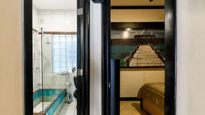 Un baño con cabina de ducha de vidrio, bañera y cama con vista a una terraza de madera a través de una puerta de vidrio.