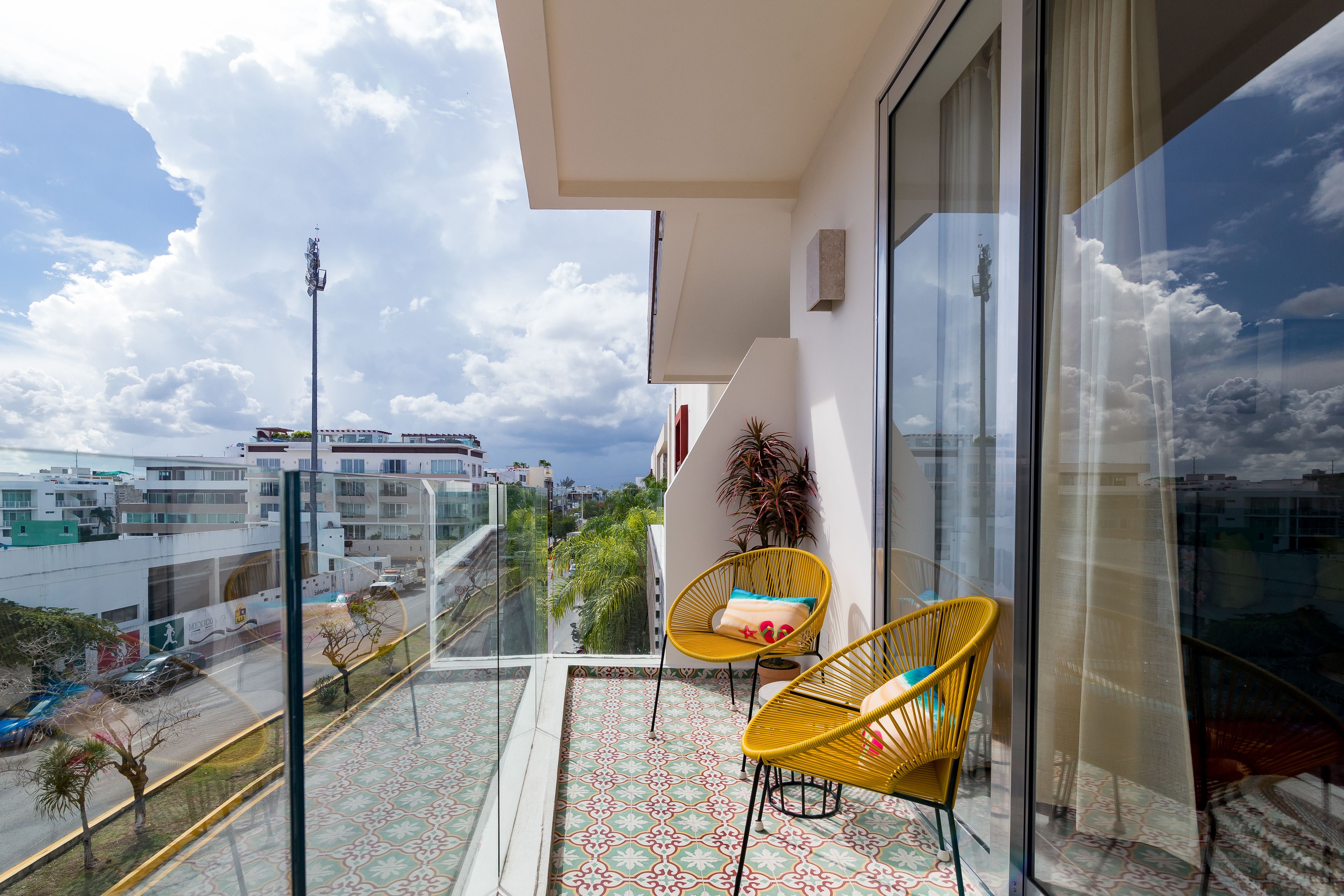 A balcony with two wicker chairs, a patterned floor, and a city view.