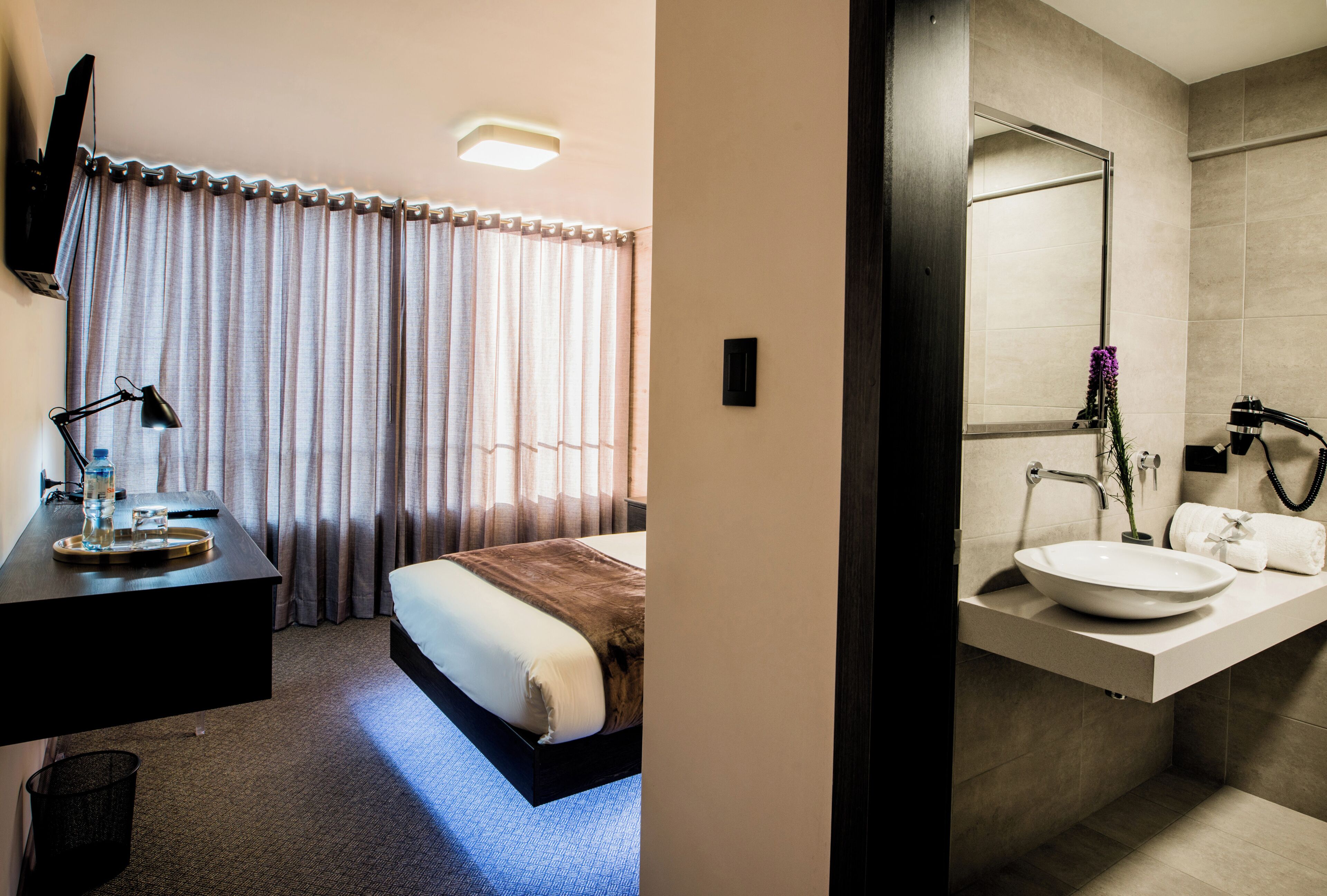 A hotel room with a bed, bedside table, lamp, and curtains.