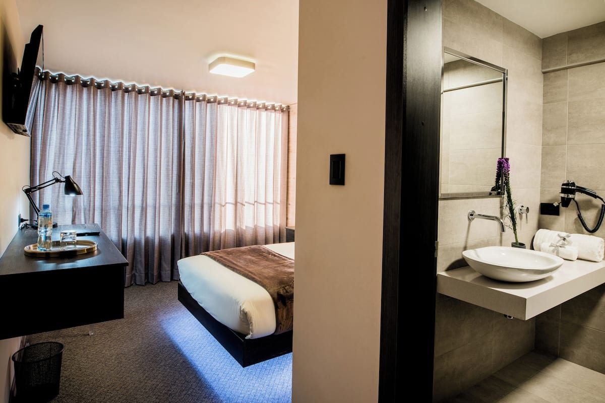 A hotel room with a bed, bedside table, lamp, and curtains.