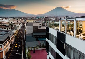 A high-rise hotel with multiple floors, a rooftop terrace, and a view of a cityscape with mountains in the background.