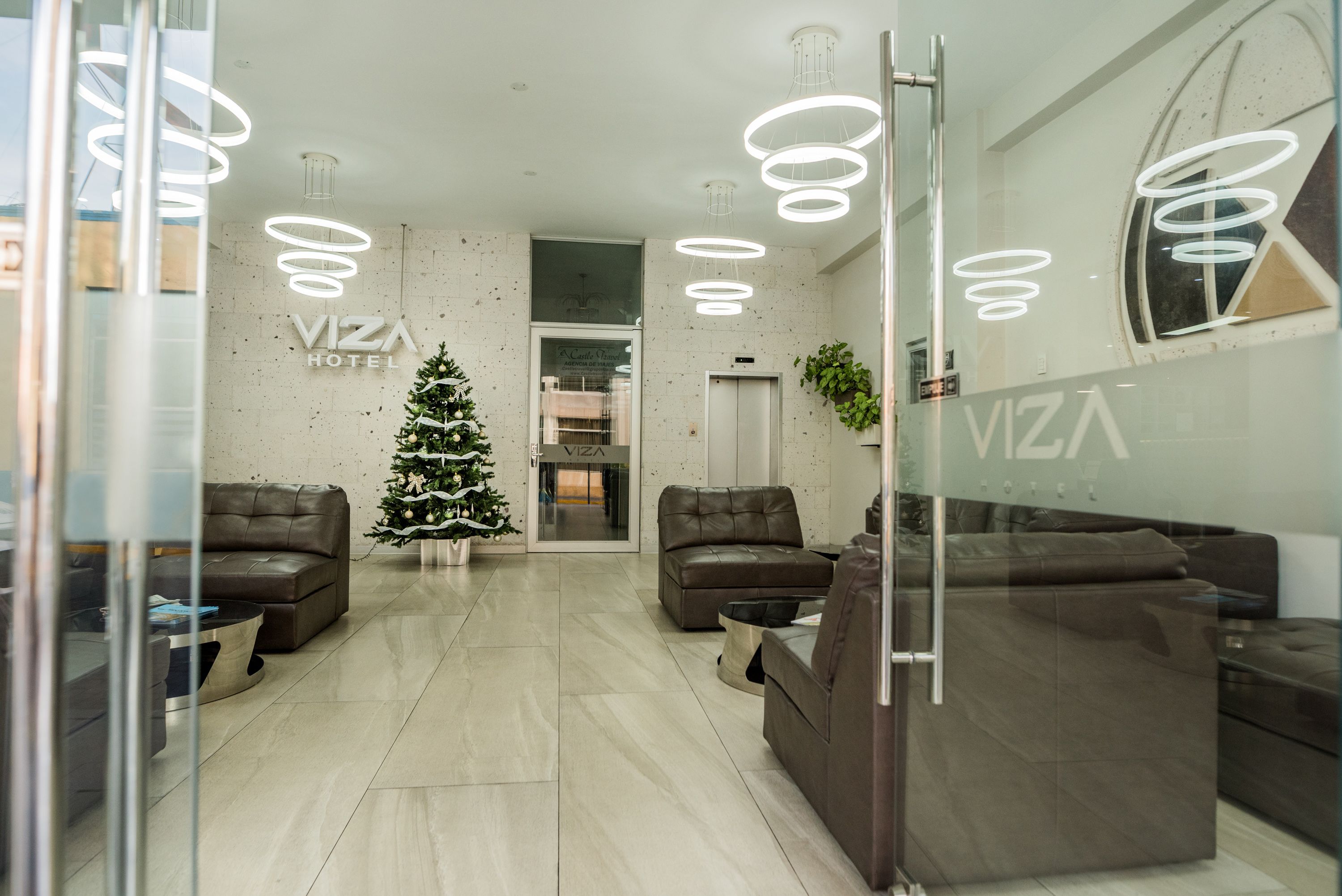 A modern lobby with leather sofas, a Christmas tree, and a Viza Hotel sign.