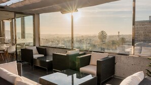 Um lounge no terraço com sofá, cadeiras e uma mesa, com vista para a cidade.