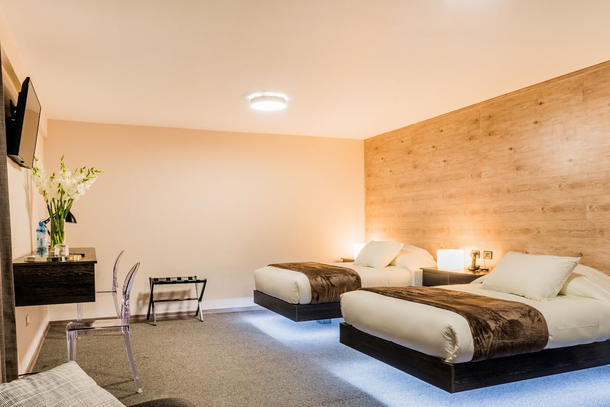A modern bedroom with two beds, a wooden accent wall, a small desk, and a chair.