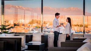 Um bar no terraço com móveis de vime e vista para a cidade.