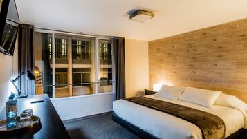 Una habitación de hotel con una cama, un escritorio con lámpara, un televisor y una ventana con cortinas.