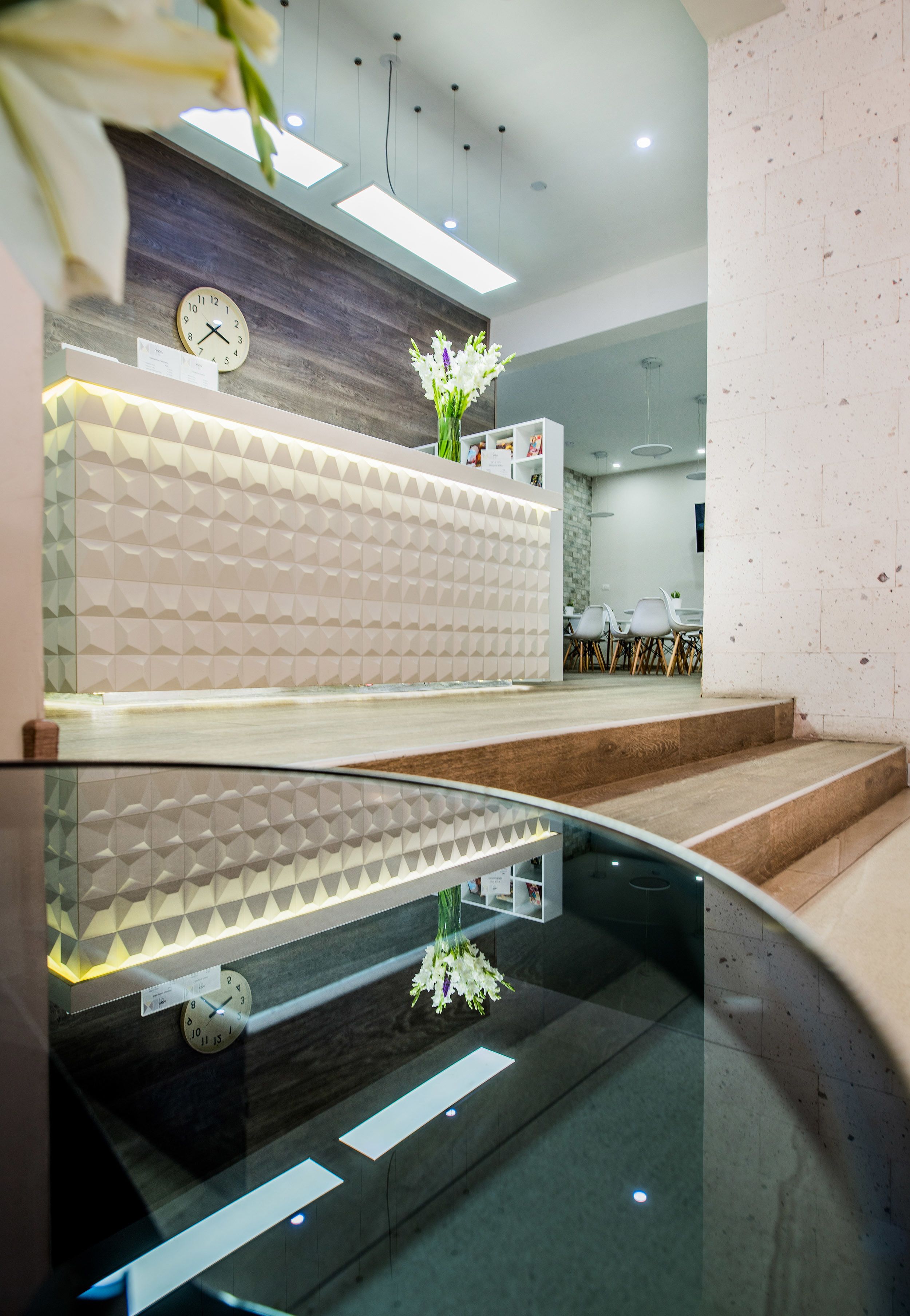 Un espace d’accueil moderne agrémenté d’une horloge, d’un vase de fleurs et d’une table en verre qui reflète l’intérieur.
