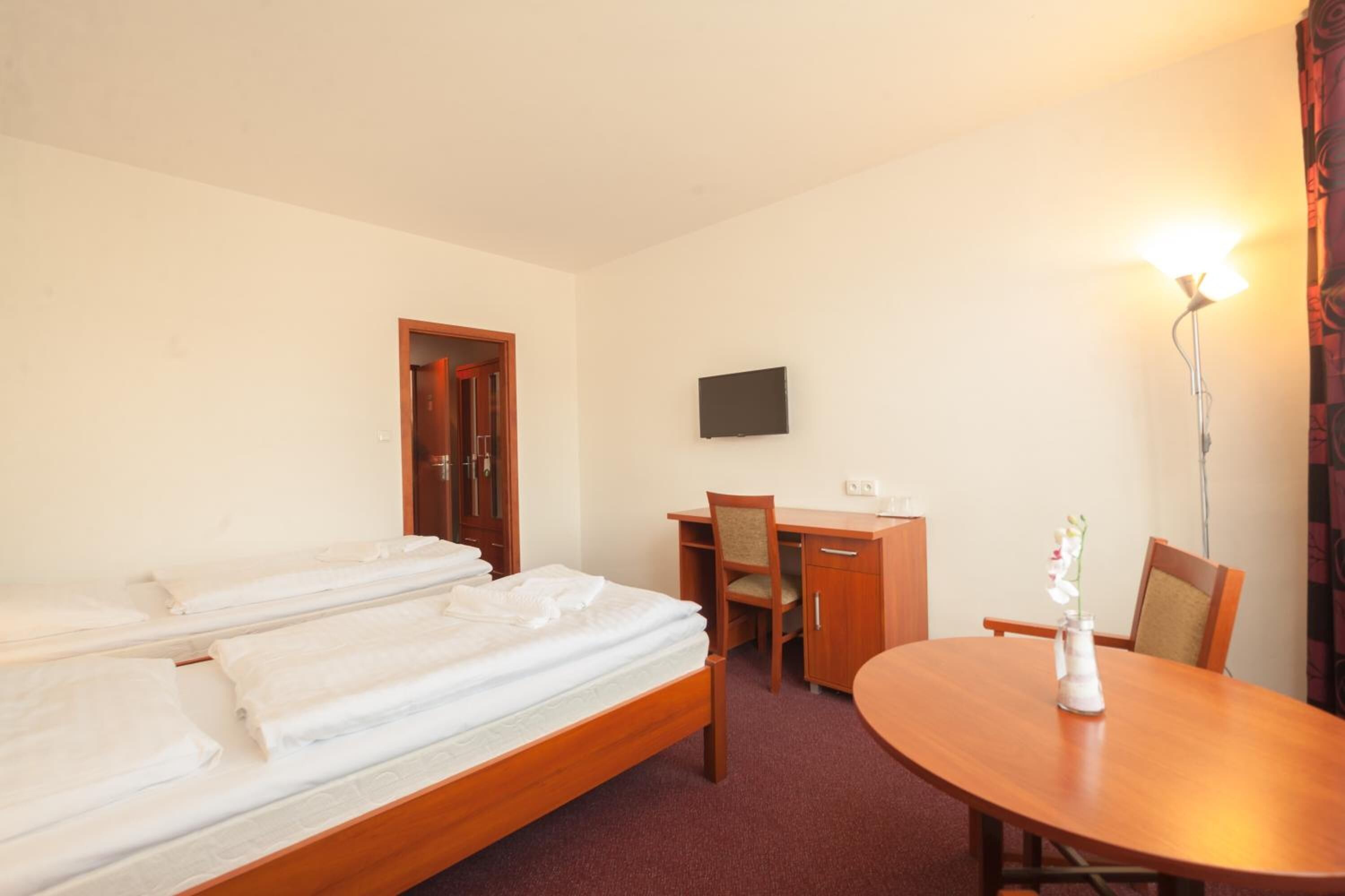 Habitació d'hotel amb un llit, una taula de treball, una cadira, un televisor i una taula amb un vas.