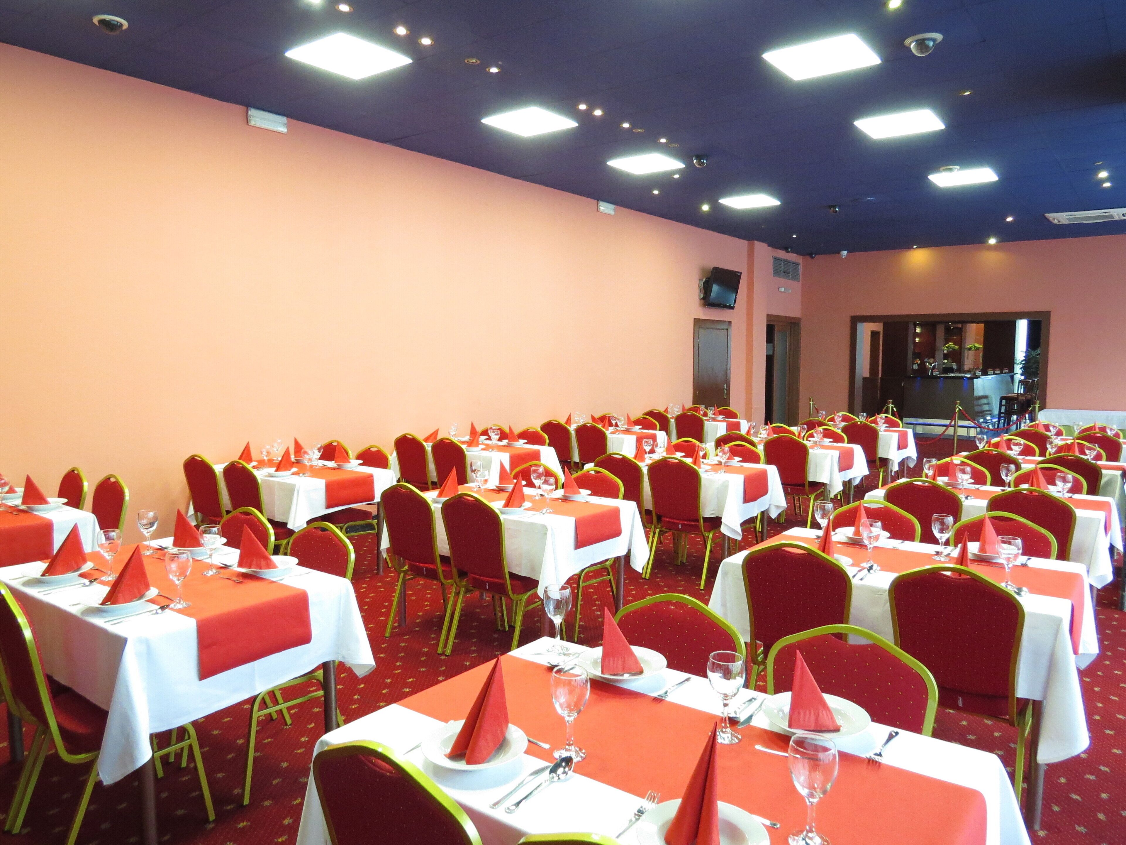 A banquet hall with multiple tables set for dining, each with red napkins, white tablecloths, and red chairs.