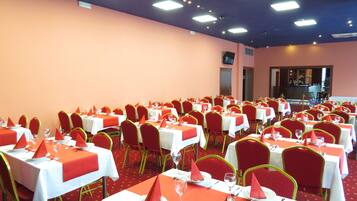 A banquet hall with multiple tables set for dining, each with red napkins, white tablecloths, and red chairs.