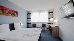 Habitación de hotel con una cama grande, un escritorio, dos sillas, un televisor y una ventana con cortinas.