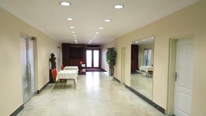 Un pasillo de hotel con mostrador de recepción, zona de recepción y comedor con mesas y sillas.