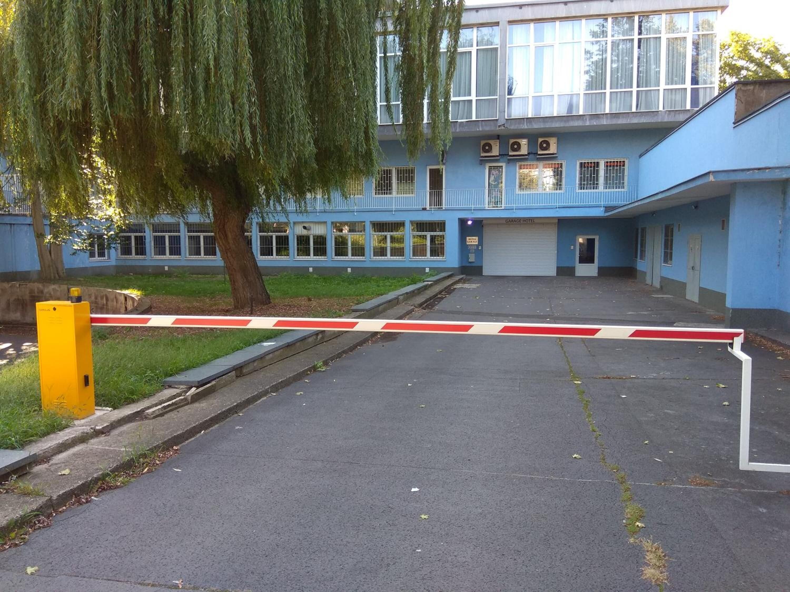 Un edificio azul con entrada de garaje, un árbol en la parte delantera y un bolardo amarillo.