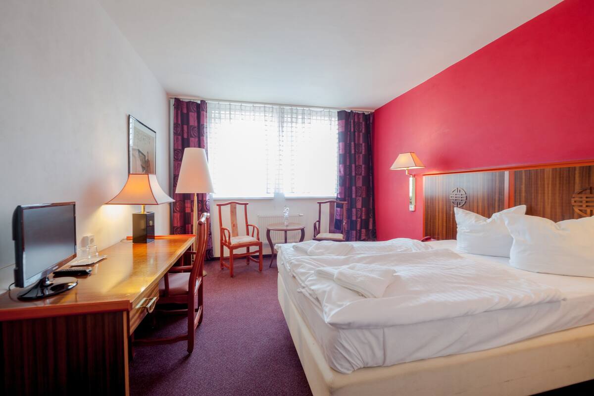 Una habitación de hotel con cama, escritorio, sillas y televisor.