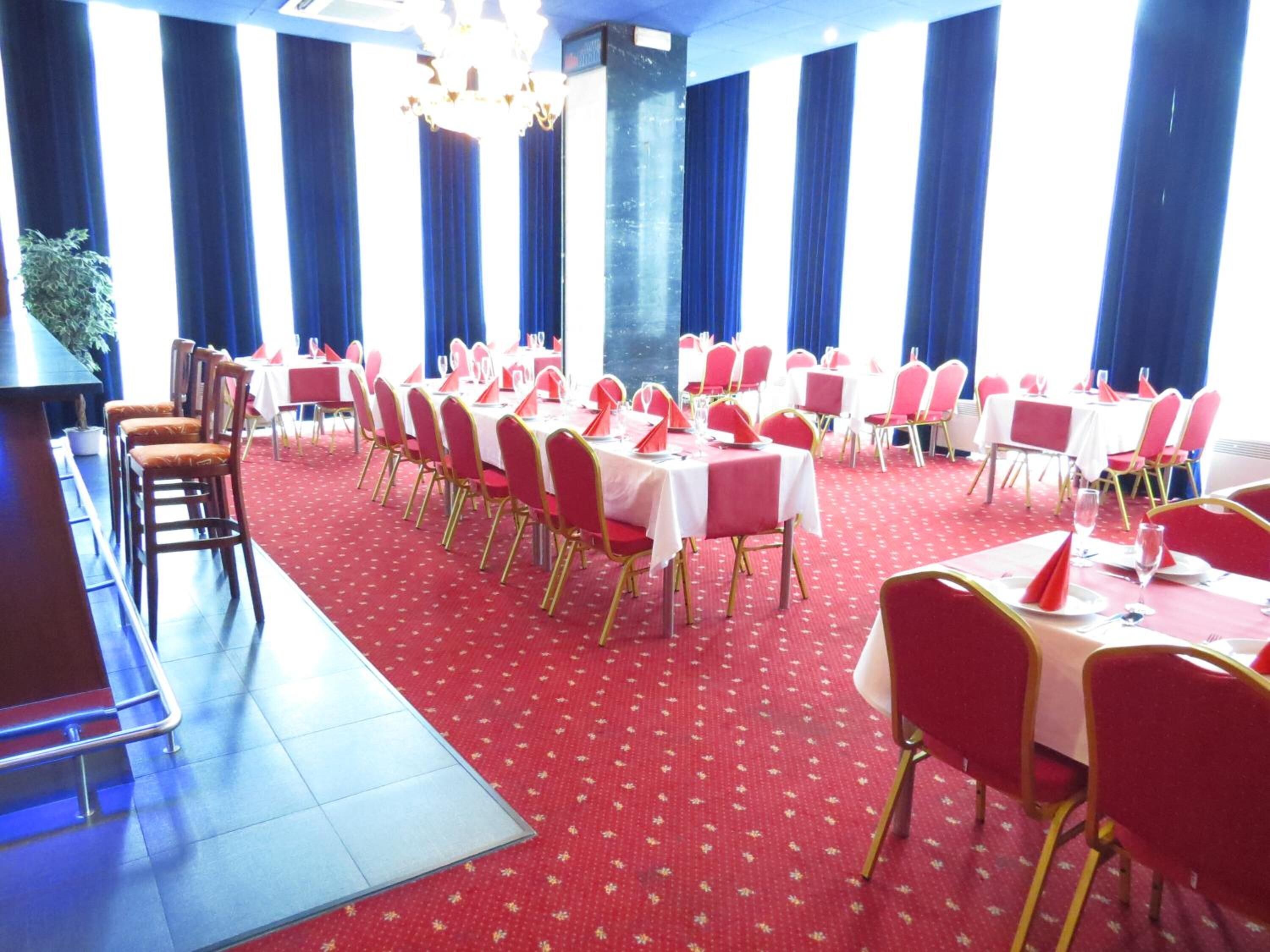 A banquet hall with round tables, red and white tablecloths, and gold chairs.