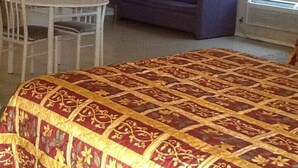 Une pièce comprenant un lit, une petite table, une chaise, un canapé et une fenêtre avec des stores.