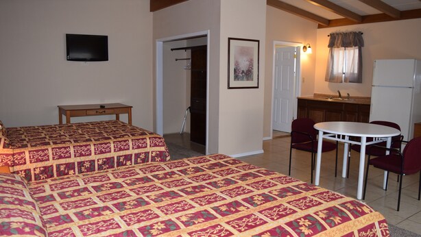 Une chambre d’hôtel avec deux lits, une petite table, une chaise, un bureau, une télévision, une salle de bain et une kitchenette.