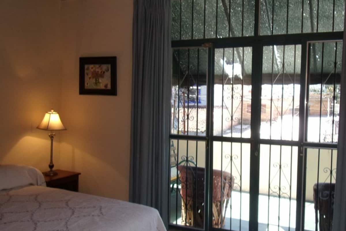 Ein Hotelzimmer mit einem Bett, einer Lampe, einer blauen Kommode und einem großen Fenster mit Metallgitter.