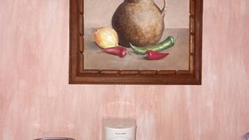 A kitchen counter with a toaster, a coffee maker, a framed painting of vegetables, and a small jar.
