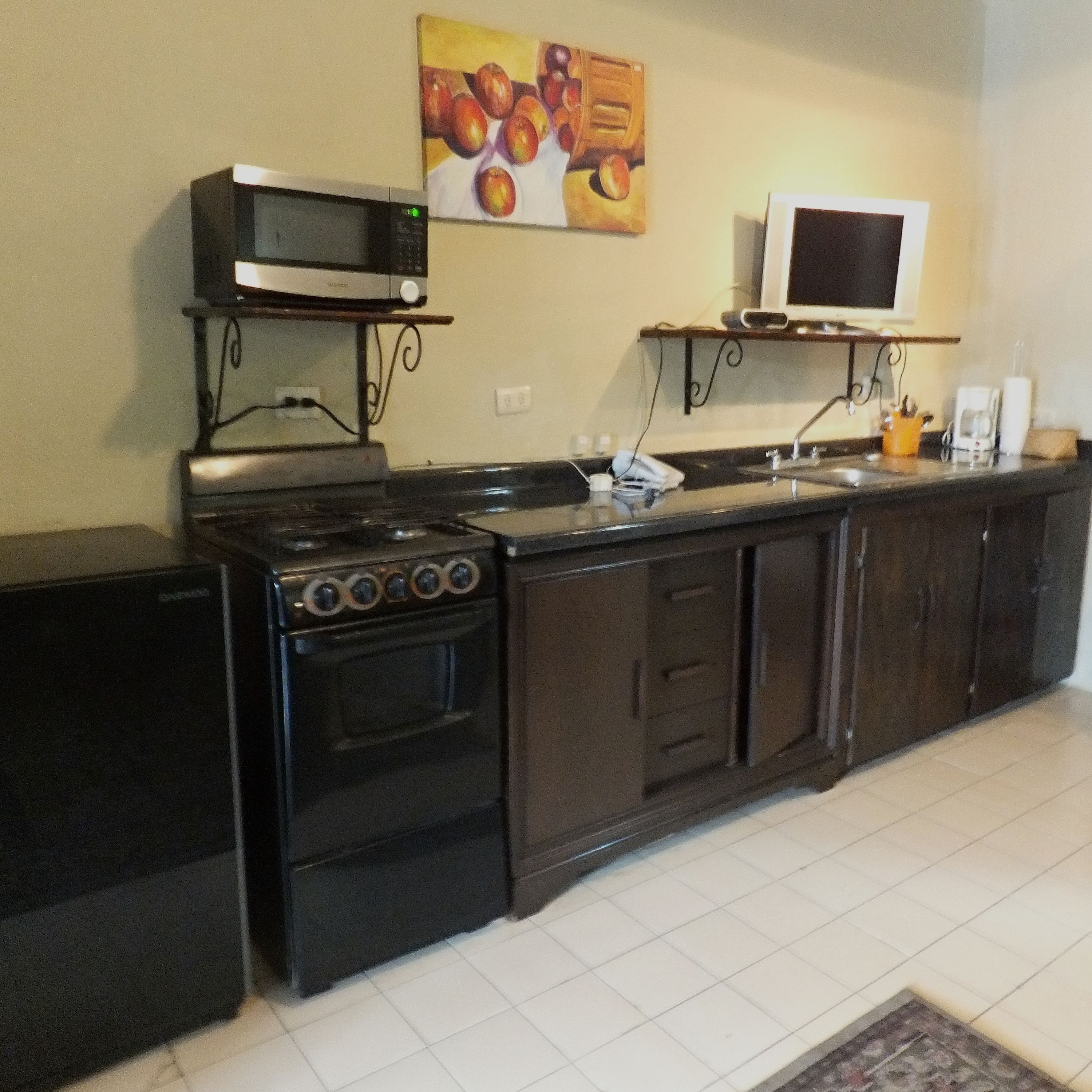 Una cocina compacta con estufa, horno, microondas y un pequeño televisor en un estante.